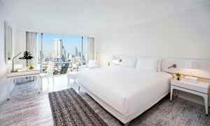 Hotelværelse med moderne indretning, stor seng og udsigt over byens skyline gennem store vinduer. (AI-genereret tekst)