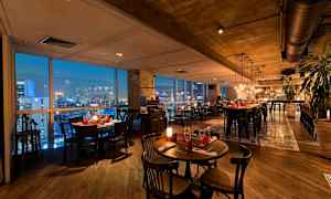 En elegant restaurant med moderne møbler, vinduer der viser en byudsigt om aftenen og belysning, der skaber en hyggelig atmosfære. (AI-genereret tekst)