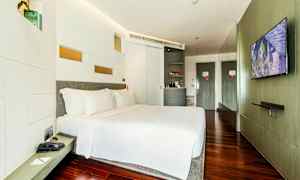 Et moderne hotelværelse med en stor seng, hvidt sengelinned og trægulv. Et TV er monteret på væggen overfor sengen, og der er en minibar samt et skab i rummet. (AI-genereret tekst)