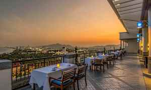 En terrasse med spisebord og stole opsat, omgivet af udsigt over en by ved solnedgang. (AI-genereret tekst)