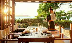 Udsigt over et dækket bord på en udendørsrestaurant med solnedgang i baggrunden. (AI-genereret tekst)