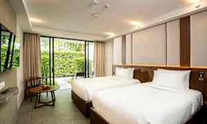 Et hotelværelse med to enkeltsenge med hvidt sengetøj, et vindue med udsigt over en have og et træbord med en stol ved siden af. (AI-genereret tekst)