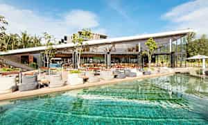 En moderne café eller restaurant med store glasvægge ligger ved en pool under en klar blå himmel. (AI-genereret tekst)