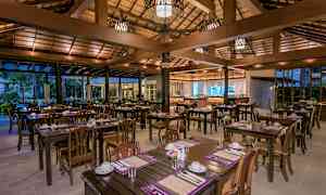 En åben restaurant med træborde og stole, dækket til måltider. (AI-genereret tekst)