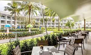 Restaurant med udendørs servering ved en have med græsarealer og legeområde. (AI-genereret tekst)