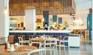 Billede af en restaurant med moderne interiør og blå fliser, hvor træborde og stole er arrangeret rundt omkring. (AI-genereret tekst)