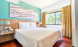 Et hotelværelse med en dobbeltseng, store vinduer og gardiner. (AI-genereret tekst)