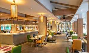 Interiør af en restaurant med borde og stole i forskellige farver samt hængende lamper. (AI-genereret tekst)