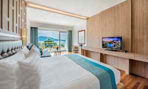 Et hotelværelse med en stor seng, et fjernsyn og en balkon med udsigt over omgivelserne. (AI-genereret tekst)