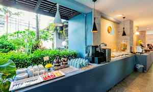 Buffetbord med kaffe, kopper, tallerkener og tropisk grønt i baggrunden. (AI-genereret tekst)