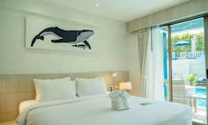 Et hotelværelse med en dobbeltseng, dekoreret med håndklæder og et maleri af en hval på væggen. Værelset har et vindue med udsigt til en pool. (AI-genereret tekst)