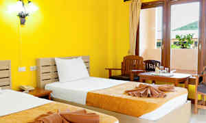 Et hotelværelse med gule vægge, to senge med gulorange sengetæpper og et vindue med udsigt. (AI-genereret tekst)