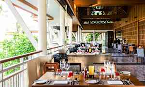 Restaurant med opdækkede borde og vinduer med udsigt til grønt område. (AI-genereret tekst)