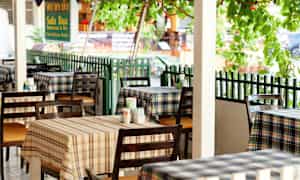 Billede af en restaurant med ternede duge og borde placeret udenfor. (AI-genereret tekst)