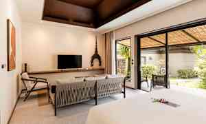 Et hotelværelse med moderne indretning, en siddegruppe, en TV og store glasdøre, der fører ud til en frodig terrasse. (AI-genereret tekst)