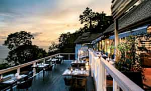 Udendørs terrasse med borde og stole om aftenen, med udsigt over træer og havet. (AI-genereret tekst)