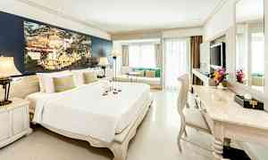 Et lyst og elegant hotelværelse med en stor seng, siddeområde ved vinduet og et skrivebord med stol. (AI-genereret tekst)