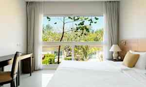 Et hotelværelse med en stor seng, et skrivebord og et vindue, der viser træer og bygninger udenfor. (AI-genereret tekst)