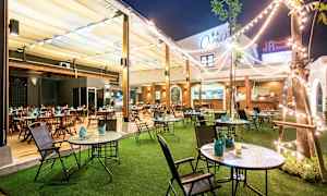 En udendørs restaurant med borde og stole, græsplæne og lyskæder. (AI-genereret tekst)