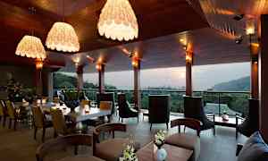 En moderne restaurant eller lounge med elegant indretning, store vinduer og udsigt over en skov og bakker i baggrunden. (AI-genereret tekst)