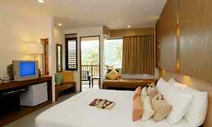 Et hotelværelse med en stor seng, flere puder, et fjernsyn, en siddegruppe og en altan med udsigt over palmer og bjerge. (AI-genereret tekst)