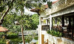 En terrasse i en tropisk haveomgivelser med frodig grønt og en lille dam. (AI-genereret tekst)