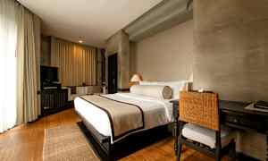 Et hotelværelse med en stor redt seng, skrivebord med stol og et fjernsyn i et hyggeligt og lyst indrettet rum. (AI-genereret tekst)