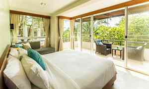 Et lyst og rummeligt soveværelse med en stor seng, sofagruppe og en balkon med udsigt over grønt. (AI-genereret tekst)