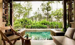 En åben stue med træstole og bord, en sofa, og udsigt til en have og en lille pool. (AI-genereret tekst)