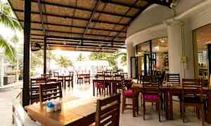 En udendørs restaurant med tag og træborde placeret på en stor terrasse. (AI-genereret tekst)