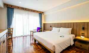 Et hotelværelse med en dobbeltseng, mørkt trægulv og et stort vindue med blå gardiner og hvidt voile. (AI-genereret tekst)