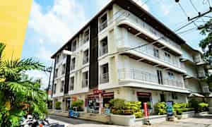 Billede af en hvid bygning med flere etager, omgivet af grønne planter og motorcykler parkeret ved siden af. (AI-genereret tekst)