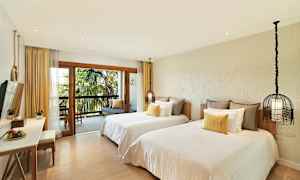 Hotelværelse med to separate senge, en balkon med udsigt over palmer og en siddegruppe. (AI-genereret tekst)