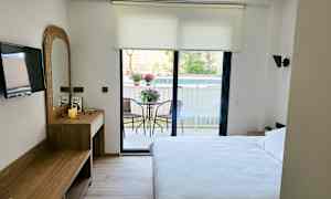 Et hotelværelse med en dobbeltseng, skrivebord, TV og en altan med havemøbler. (AI-genereret tekst)