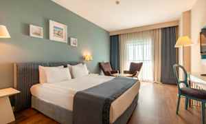 Et hotelværelse med en dobbeltseng, to lænestole ved et bord, et skrivebord og et fjernsyn. (AI-genereret tekst)