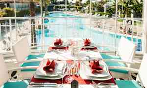 Et bord dækket med røde servietter og hvide tallerkener ved en swimmingpool. (AI-genereret tekst)