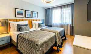 Et hotelværelse med to enkeltsenge, moderne indretning og naturligt lys fra et vindue. (AI-genereret tekst)