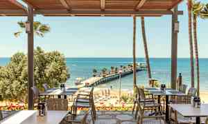 En restaurant med udsigt over en strand og en mole, der strækker sig ud i havet. (AI-genereret tekst)