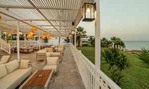 Udendørsområde med siddegrupper og udsigt over grønt areal samt hav. (AI-genereret tekst)