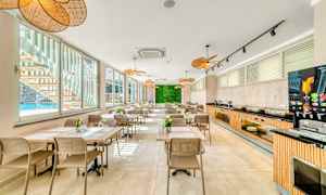 Et moderne og lyst spiseområde med mange borde og siddepladser, store vinduer med udsigt til en pool og en plantevæg for enden. (AI-genereret tekst)