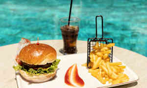 En burger, pommes frites og et glas sodavand på et bord ved en pool. (AI-genereret tekst)
