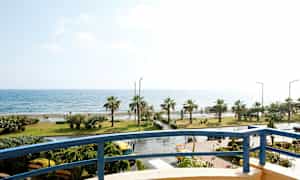 Udsigt fra en altan mod en kystlinje med palmer og hav. (AI-genereret tekst)