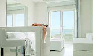 Et lyst, moderne rum med hvide møbler, store vinduer med udsigt til havet og dekorative detaljer på en bordflade. (AI-genereret tekst)