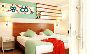 Værelse med en dobbeltseng, to grønne puder, et rødt tekstil og vægdekoration. (AI-genereret tekst)