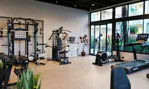 Et fitnessrum med forskellige træningsmaskiner og vægte samt glasvinduer med udsigt til udendørs. (AI-genereret tekst)
