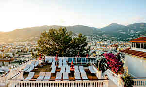 En terrasse med solsenge og parasoller samt udsigt over byen med bjerge i baggrunden. (AI-genereret tekst)