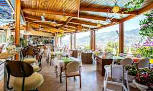 En restaurant med udsigt over bjergene og byen, med borde dekoreret med blomster. (AI-genereret tekst)