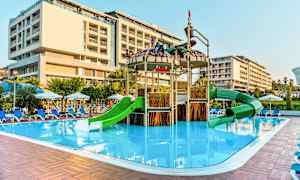 Udendørs poolområde med en legeplads med grønne rutsjebaner og et nærliggende hotel. (AI-genereret tekst)