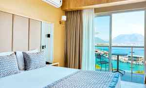 Hotelværelse med dobbeltseng, balkon med udsigt over havet og bjergene. (AI-genereret tekst)