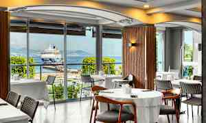 Restaurant med udsigt over et krydstogtskib ved en havn. (AI-genereret tekst)